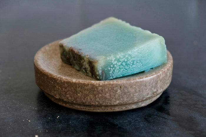 A teal soap bar on a round stone soap dish