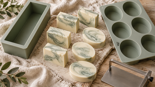 Illustrated editorial arrangement of loaf and individual-cavity silicone soap molds with cream and sage bars.